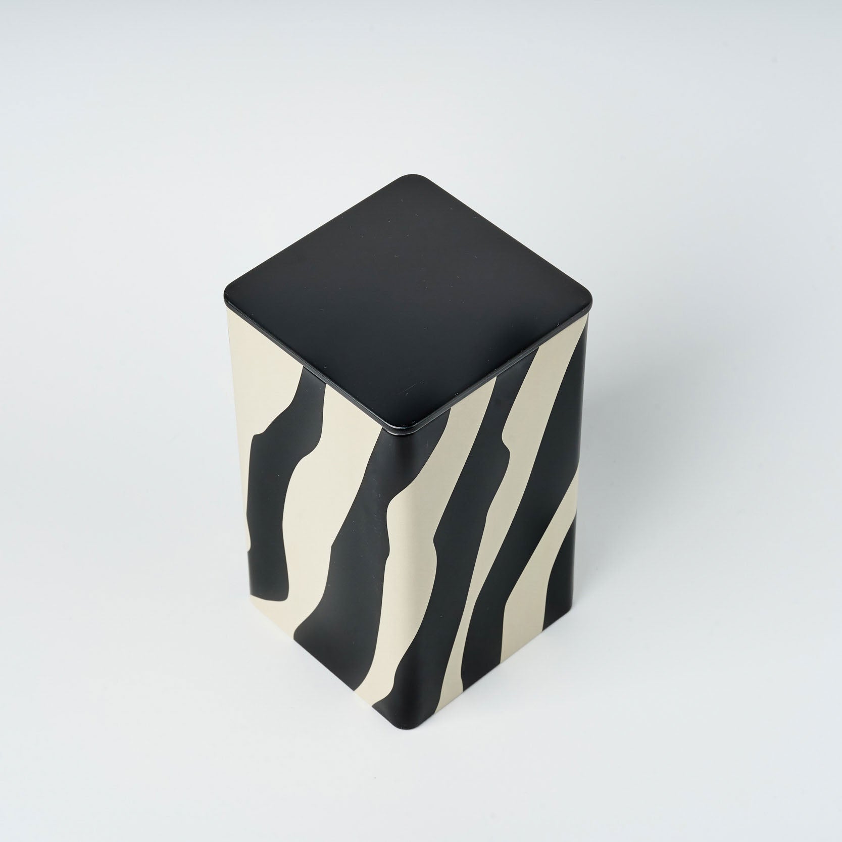 Alexander tall tin, black lid visible, black and white wavy zebra striped design.