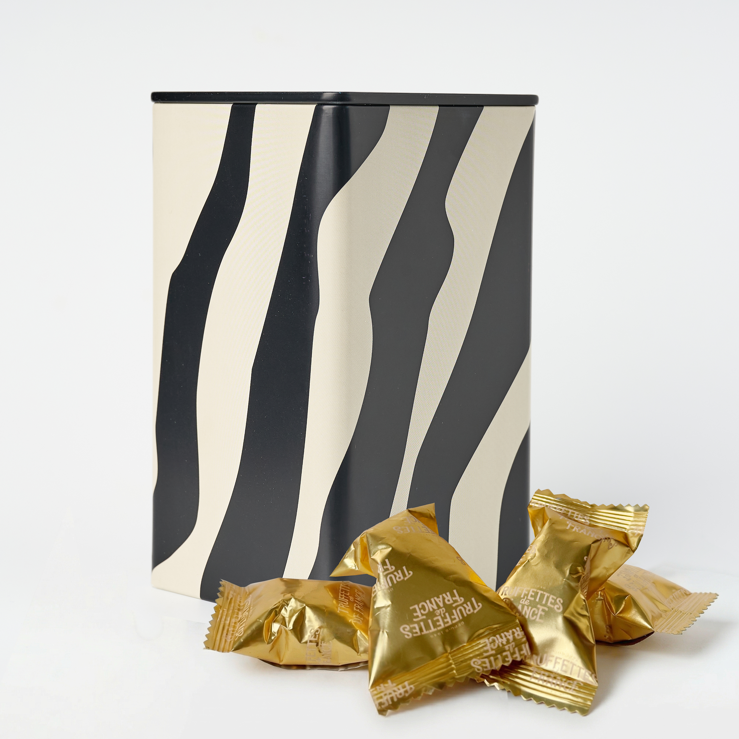 Black and white wavy striped container with gold foil wrapped chocolate truffles on a white background