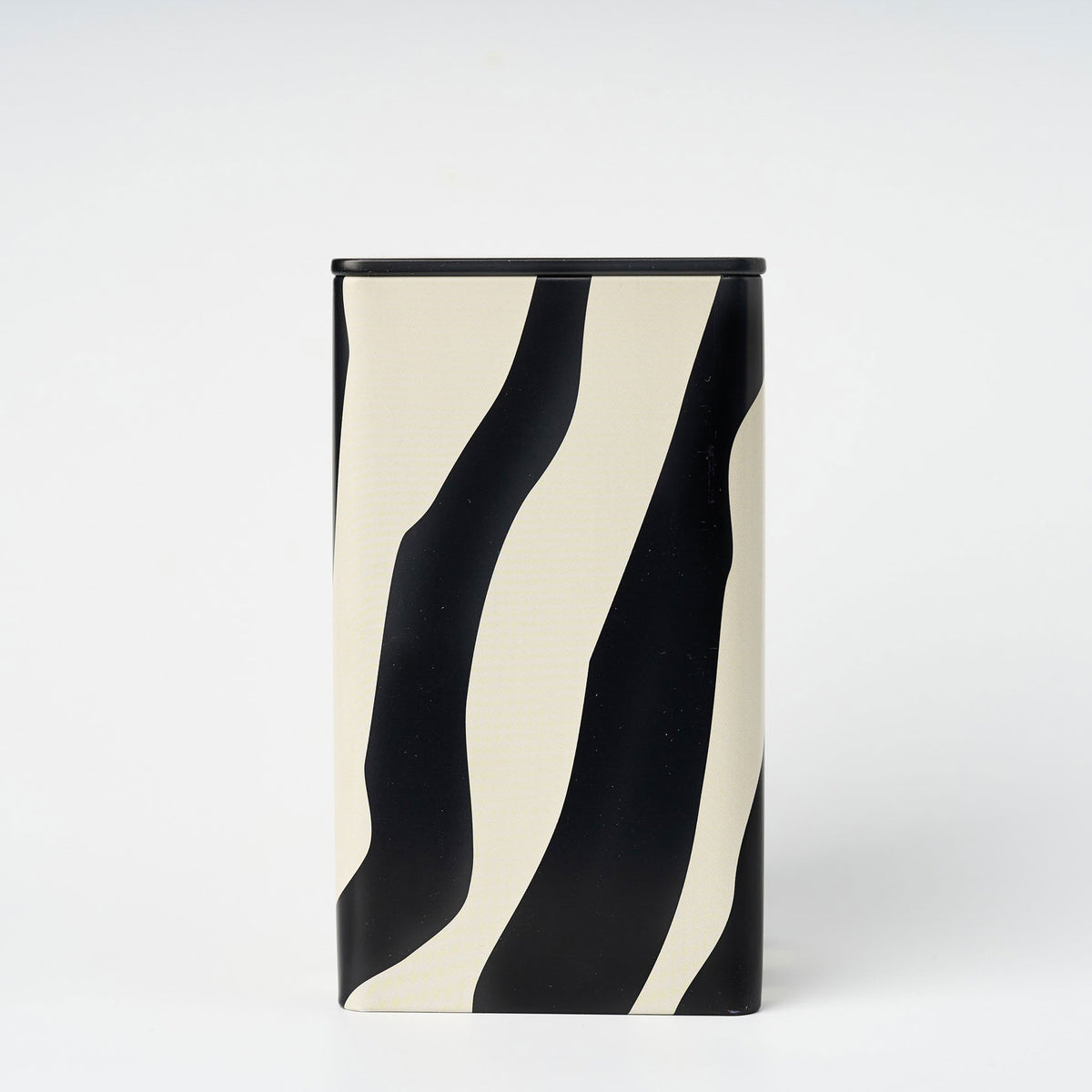 Tall rectangular tin with black and white wavy pattern set against a plain white backdrop